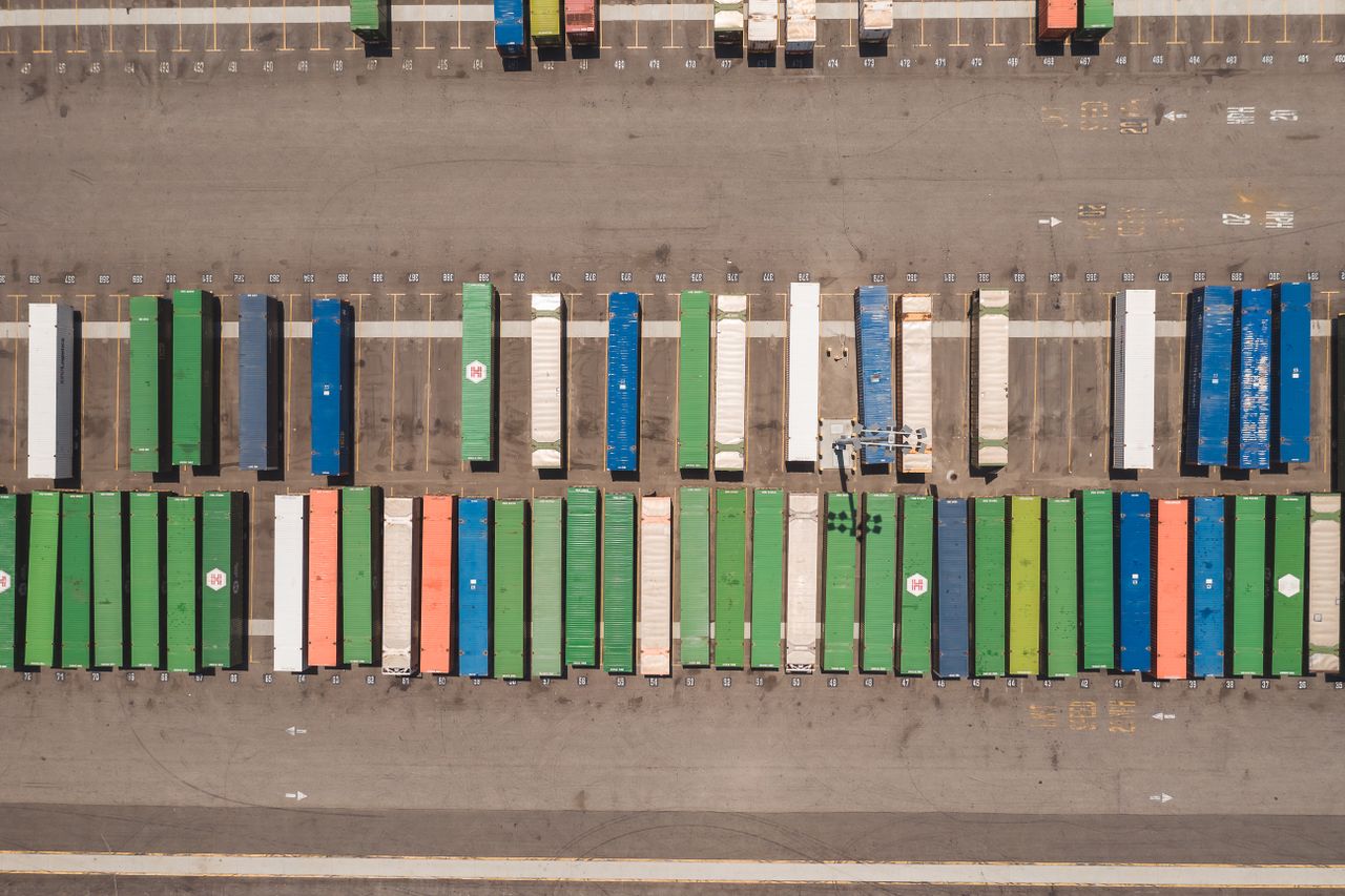 our-journey-02 Top view of neatly arranged cargo containers in a shipping port, highlighting logistics and global trade.